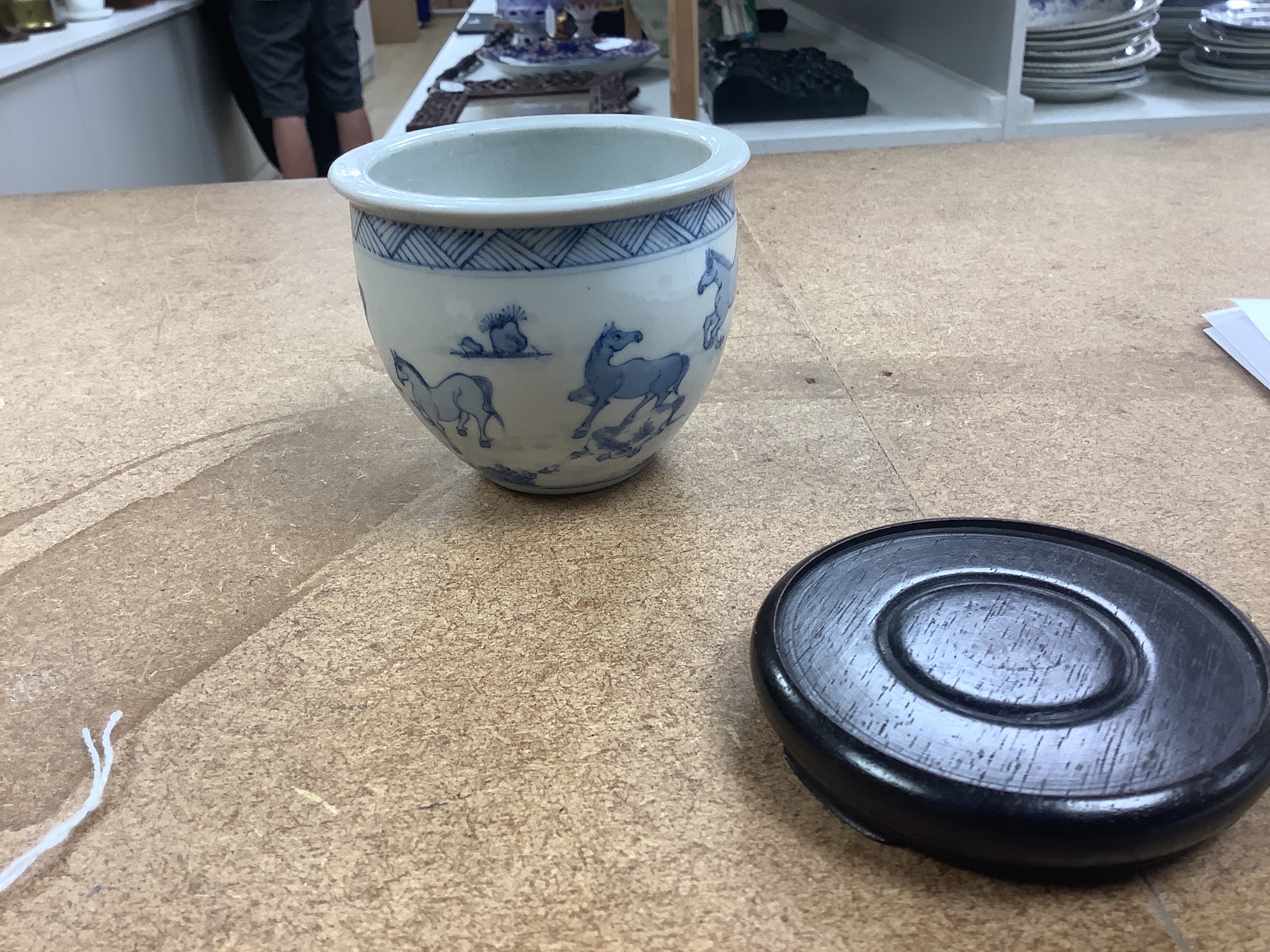 A Chinese blue and white ‘eight horses’ brush pot, on wooden stand, 8cm tall including stand